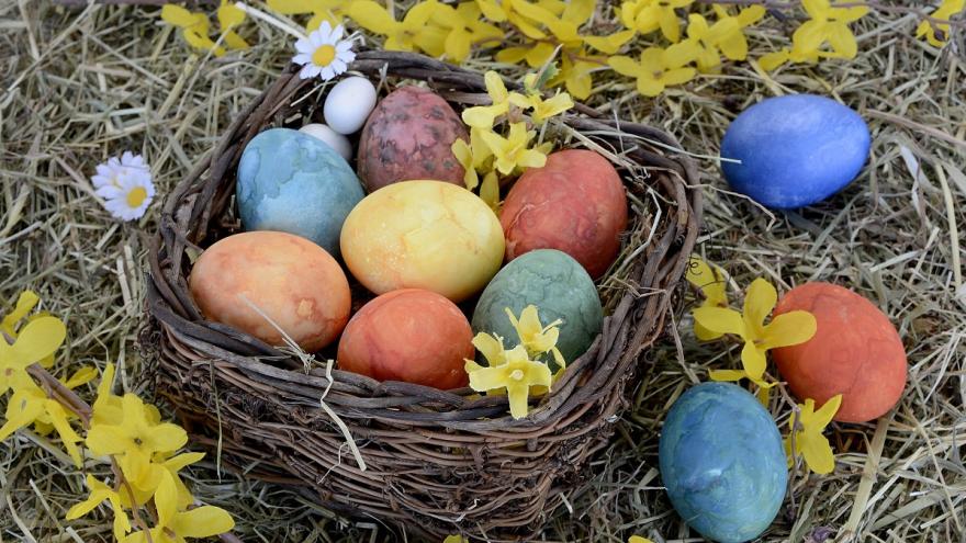 Ein Korb mit bunten Ostereiern auf einer Wiese. Um den Korb herum liegen bunte Eier und Blumen.