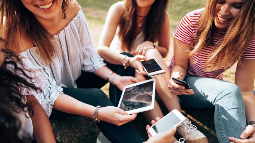 Eine Gruppe junger Frauen. Sie sitzen in einem Park und schauen auf ihre Handys und Tablets.