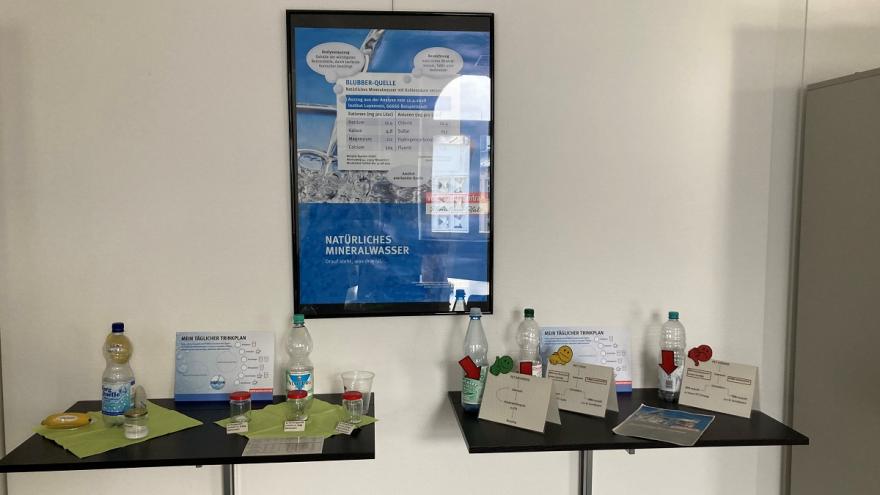 Ein Plakat. Davor zwei Tische mit Infomaterial zu Trinkwasser.