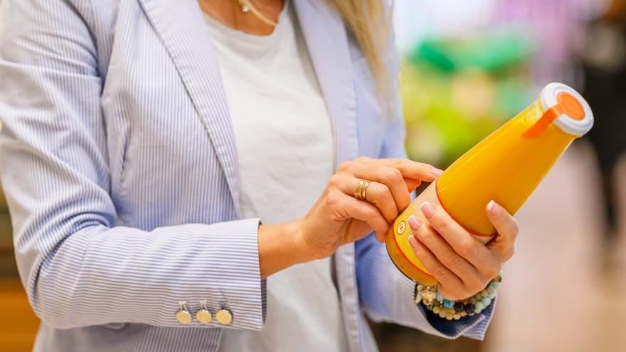 Frau im Supermarkt, die ein Etikett einer Saftflasche studiert.