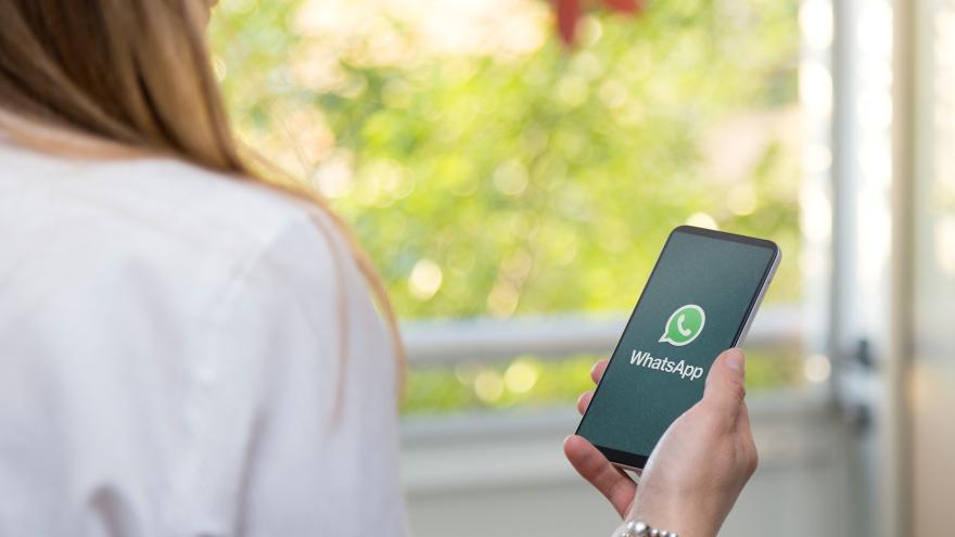 Eine Frau hält ihr Smartphone in der Hand. Auf dem Display ist das Logo von WhatsApp zu sehen. 