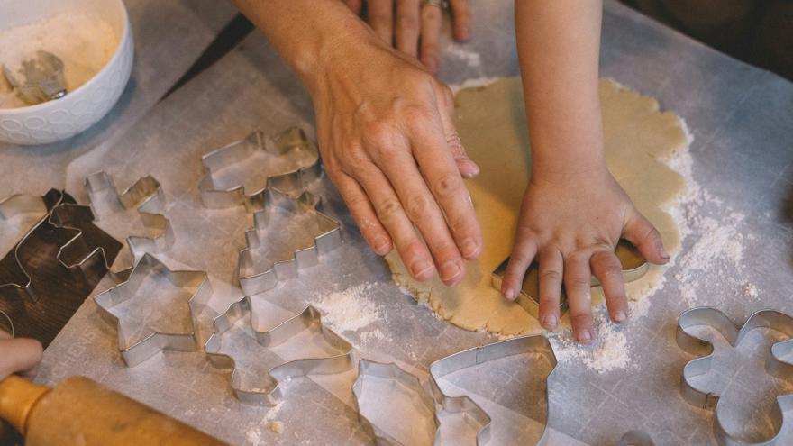 Eine große und eine kleine Hand stechen gemeinam Plätzchen aus.