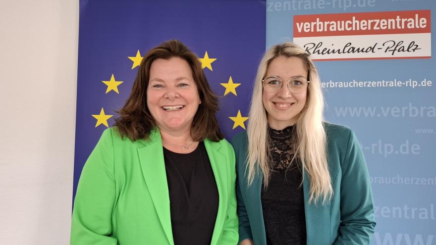 Zwei Frauen vor einem Banner mit der Europa-Flagge und lächeln in die Kamera.