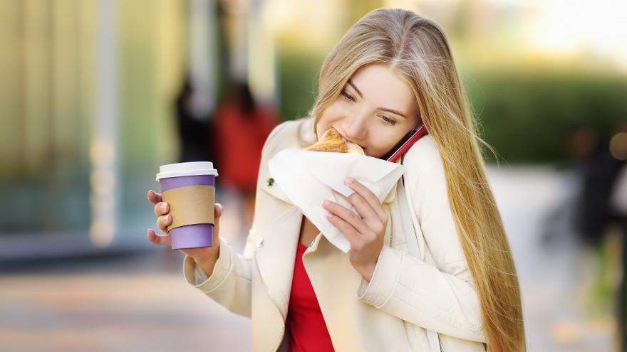 Eine Frau ist unterwegs und beißt in ein Sandwich. Inder anderen Hand hat sei einen Coffee to go in der Hand