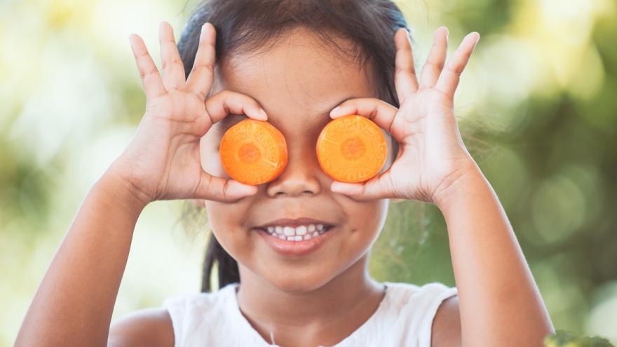 Ein Kind hält sich zwei Karottenscheiben vor die Augen und lächelt.