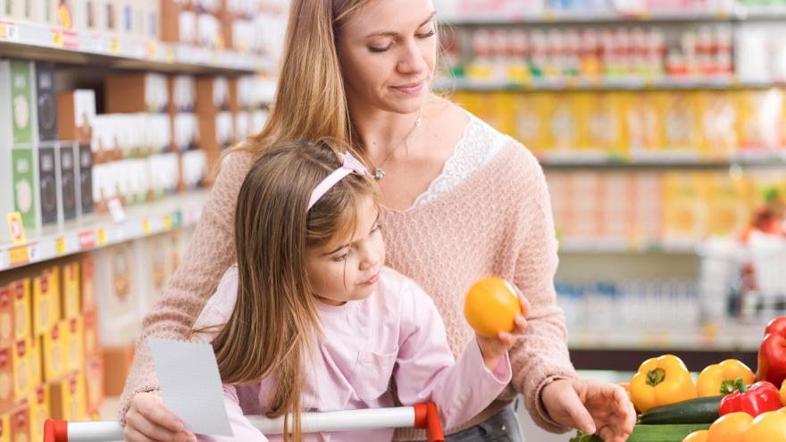 Frau und Tochter mit Einkaufswagen stehen am Obstregal.