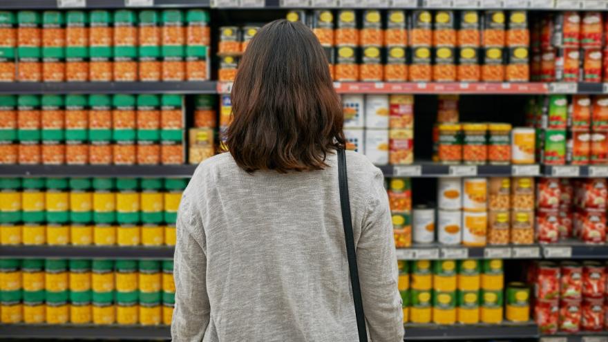 Eine Frau steht vor einem sehr großen Supermarktregal voller Fertigprodukte