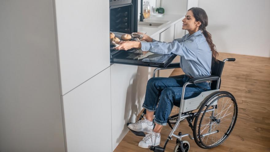 Eine Frau im Rollstuhl holt ein Backblech aus dem Backofen.