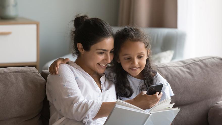 Mutter und Kind sitzen gemeinsam auf der Couch und schauen auf einen Smartphone.