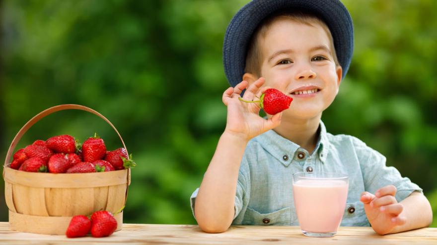 Ein Junge sitzt mit einem Glas Erdbeermilch und einem Korb Erdbeeren am Tisch