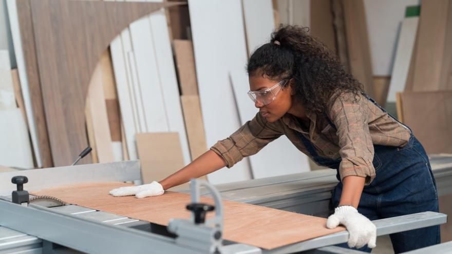 Eine Frau schneidet an einer Werkbank ein Stück Holz