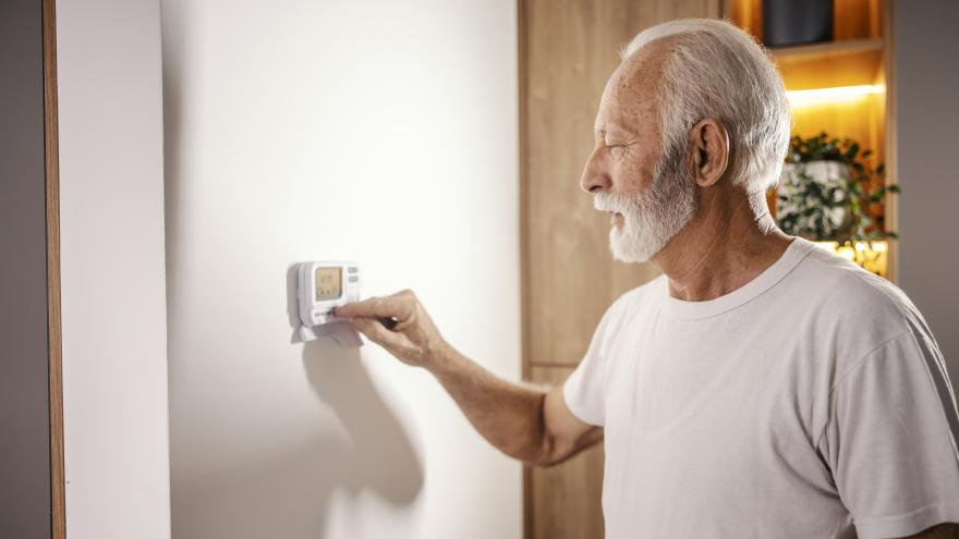 Ein älterer Mann bedient eine Klimaanlage/ Heizung an der Wand in seinem Wohnraum.