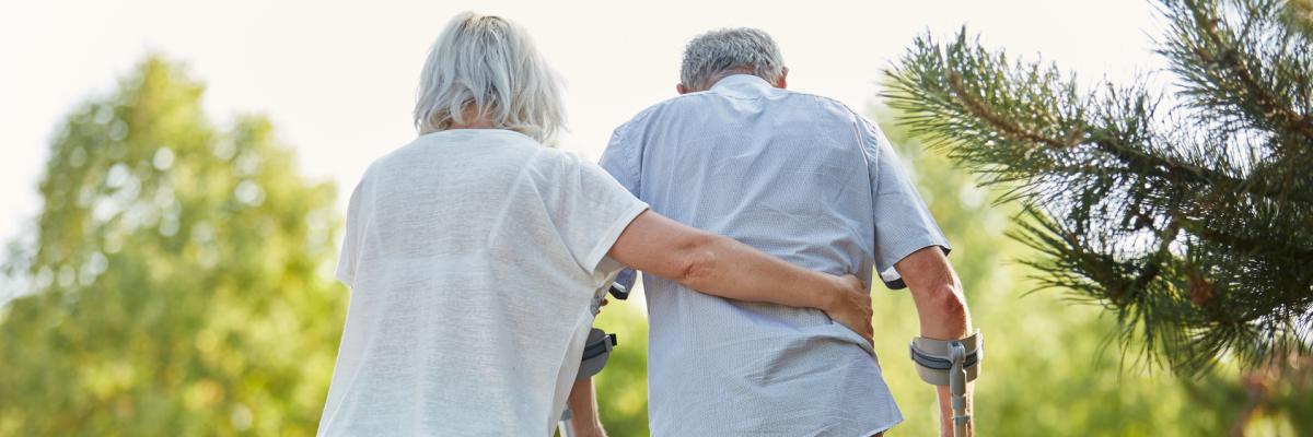 Ältere Frau pflegt älteren Mann auf Krücken