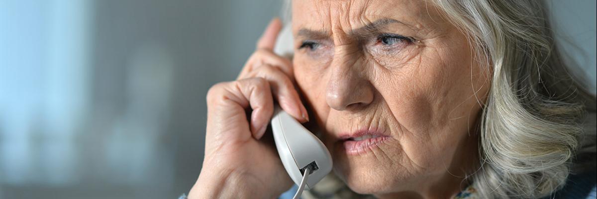 Ätere Dame hört am Telefonhörer kritisch zu