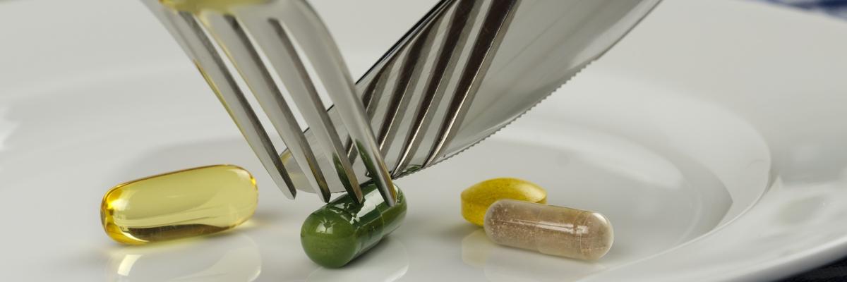 Jemand zerschneidet Schlankheits-Tabletten mit Messer und Gabel auf einem Teller