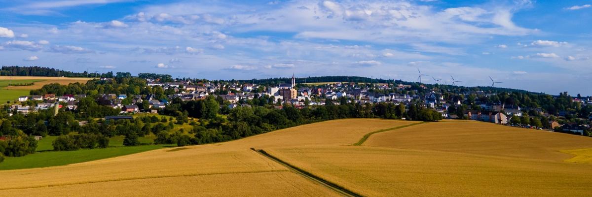 Ein weites Feld mit einem Ort im Hintergrund und blauem Himmel.