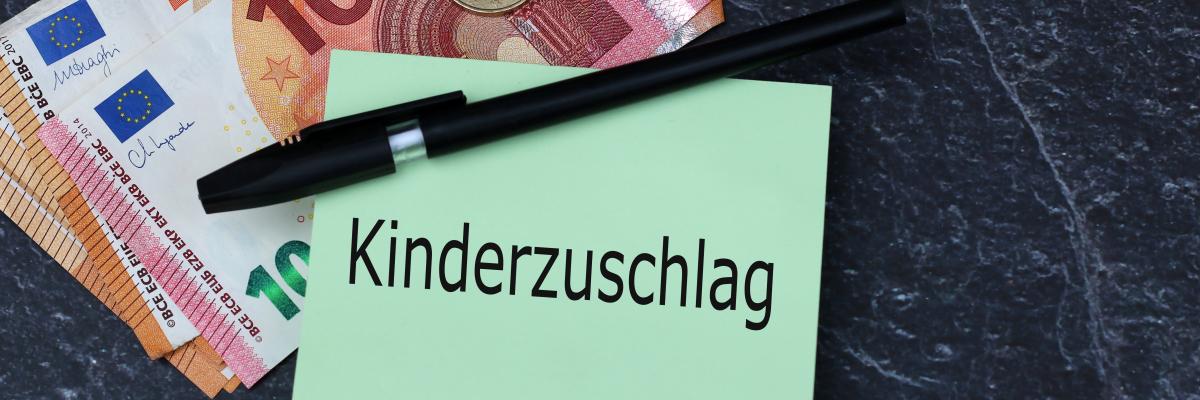 Zettel, auf dem das Wort Kinderzuschlag steht, ein Kugelschreiber sowie Geldscheine und Münzen