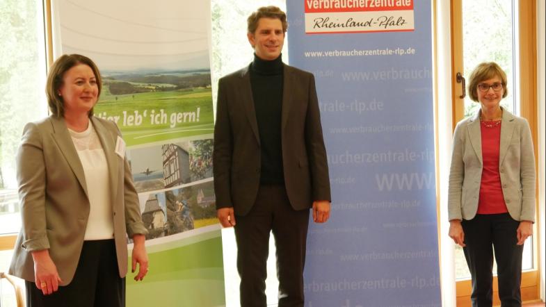 Drei Menschen stehen vor einer Wnad und blicken in die Kamera.
