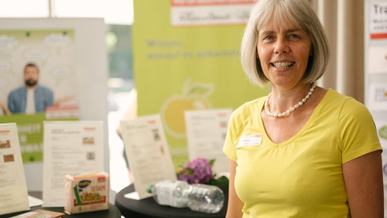 Eine Frau steht lächelnd vor einem Messestand.