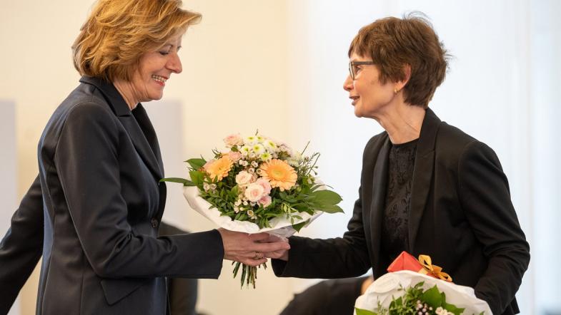 Zwei Frauen auf einer Bühne. Die eine überreicht der anderen einen Blumenstrauß.