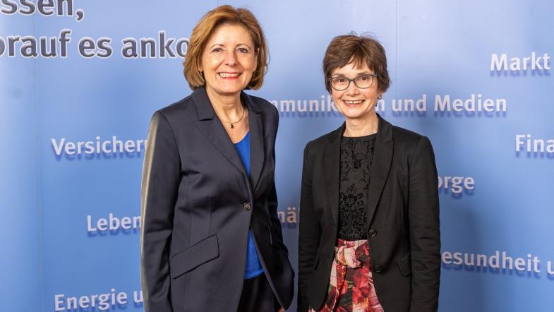 Zwei Frauen stehen vor einer blauen Wand und Blicken in die Kamera