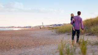 Vater mit Sohn auf dem Arm am Strand.