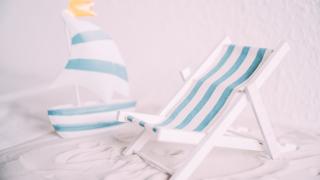 Kleiner Liegestuhl und kleines Segelboot auf Sand.