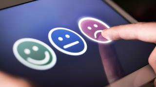 Auf einem Tablet drückt jemand auf einen unzufriedenen Smiley