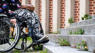Eine Person im Rollstuhl steht vor einer Treppe und kann nicht weiter fahren.