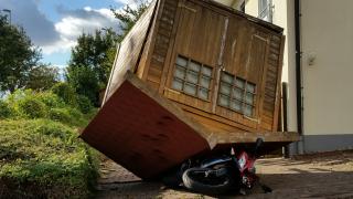 Ein Gartenhaus liegt auf dem Dach udn hat unter sich ein Motorrad begraben.