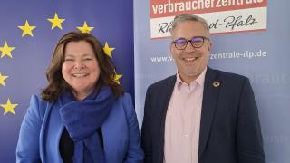 Eine Frau und ein Mann stehen vor einem Roll-up der Verbraucherzentrale und lächeln in die Kamera.