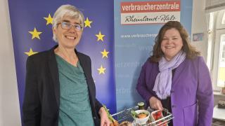 Zwei Frauen vor einem Roll-up mit der Europafahne. Sie halten einen Einkaufskorb zwischen sich.