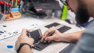 Ein Mann repariert ein Smartphone an einem Werkstatttisch.