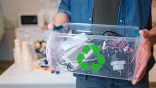 Ein Mann hält eine Plastikkiste in den Händen, die mit Elektro-Schrott gefüllt ist.