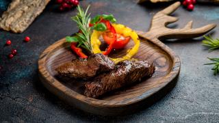 Ein Holzteller in Form eines Geweihs mit einem Stück gebratenem Wildfleisch drauf.