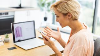 Eine Frau sitzt vor ihrem Laptop und telefoniert mit dem Kundenservice eines Onlineshops.