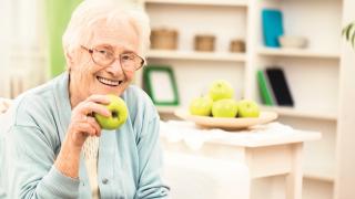 Eine Seniorin mit einem Apfel in der Hand.