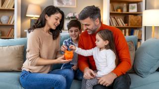 Eine Familie auf dem Sofa füttert ein Sparschwein mit Geld