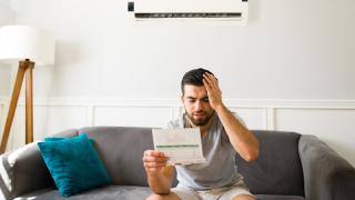 Mann sitzt auf dem Sofa und schaut auf seine hohe Stromrechnung