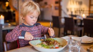 Ein Kind in einem Restaurant isst mit Messer und Gabel.