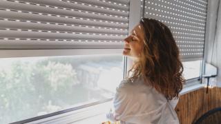 Lächelnde Frau im Wohnraum vor Fenster, Rollladen halb unten