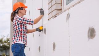 Frau in Arbeitskleidung dämmt Hausfassade