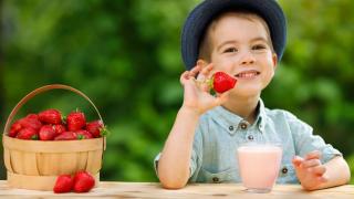 Ein Junge sitzt mit einem Glas Erdbeermilch und einem Korb Erdbeeren am Tisch