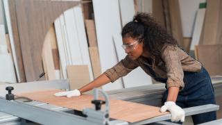 Eine Frau schneidet an einer Werkbank ein Stück Holz