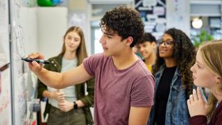 Schüler schreibt etwas auf ein Whiteboard und andere Schüler schauen zu