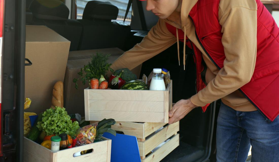 Mann räumt Lebensmittelkisten aus einem Auto-Kofferraum