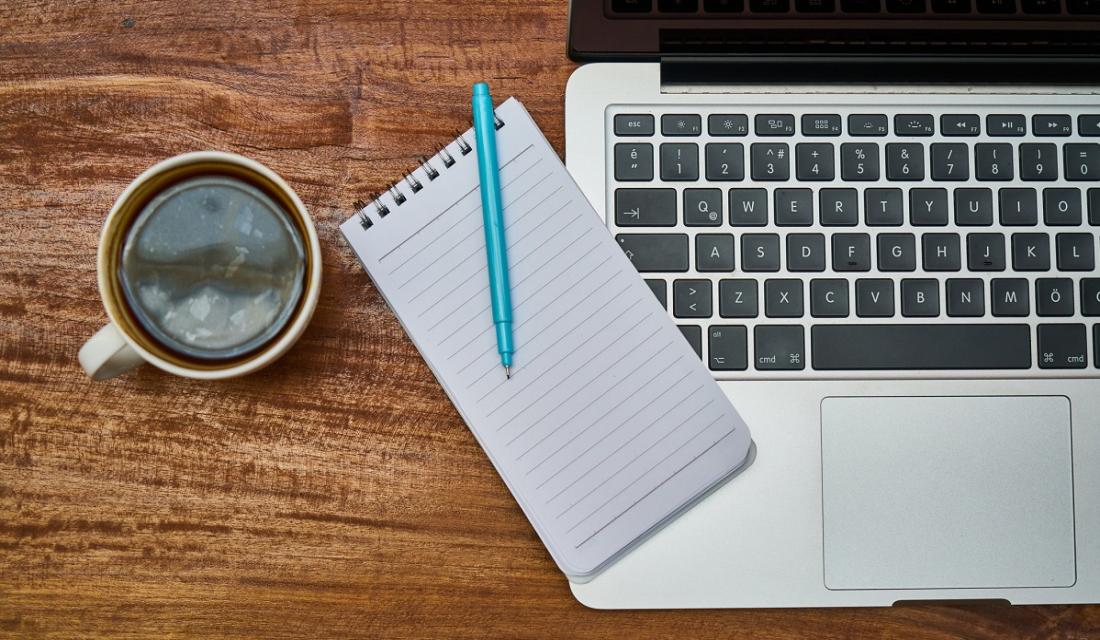 Laptop, Block und Kaffeetasse auf einem Schreibtisch